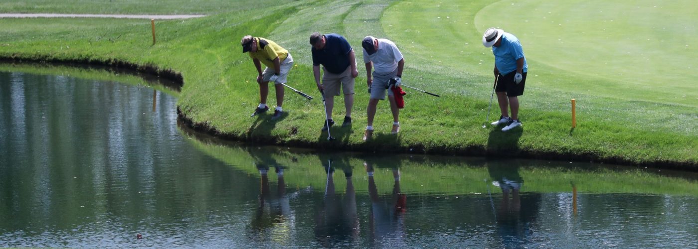 A group of golfers search for a ball that plugged into the bank of a pond